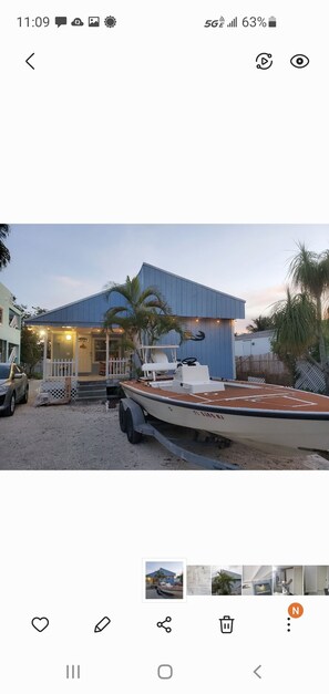 Une maison moderne avec un toit bleu, une véranda et un bateau amarré à l’extérieur.