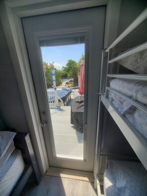 A room with a sliding door leading to an outdoor area. Inside, there are storage shelves and a bed with a patterned mattress.