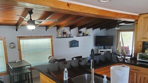 Una cucina moderna con un piano di lavoro nero, lavello in acciaio inossidabile e mobili in legno. È presente un angolo bar con sgabelli e un cartello di benvenuto.