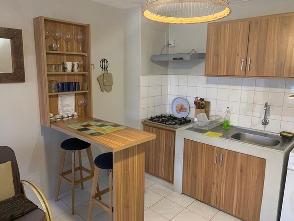 A compact kitchen with wooden cabinets, a gas stove, a sink, and a small bar area with stools.