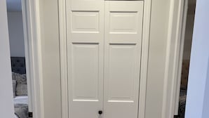 Une porte blanche fermée, dotée d’une poignée noire, et encadrée de moulures blanches, le tout reposant sur un plancher en bois.