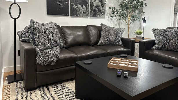 Un salon moderne avec un canapé en cuir, deux fauteuils assortis, une table basse, un lampadaire et des œuvres d’art encadrées accrochées au mur.