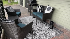 Une terrasse dotée de meubles en osier, d’un barbecue et d’un tapis à motifs.