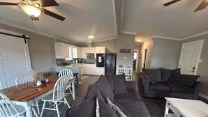 Ein modernes Wohnzimmer mit einem dunkelgrauen Ecksofa, einem Holzessttisch mit weißen Stühlen und einer Küche im Hintergrund.
