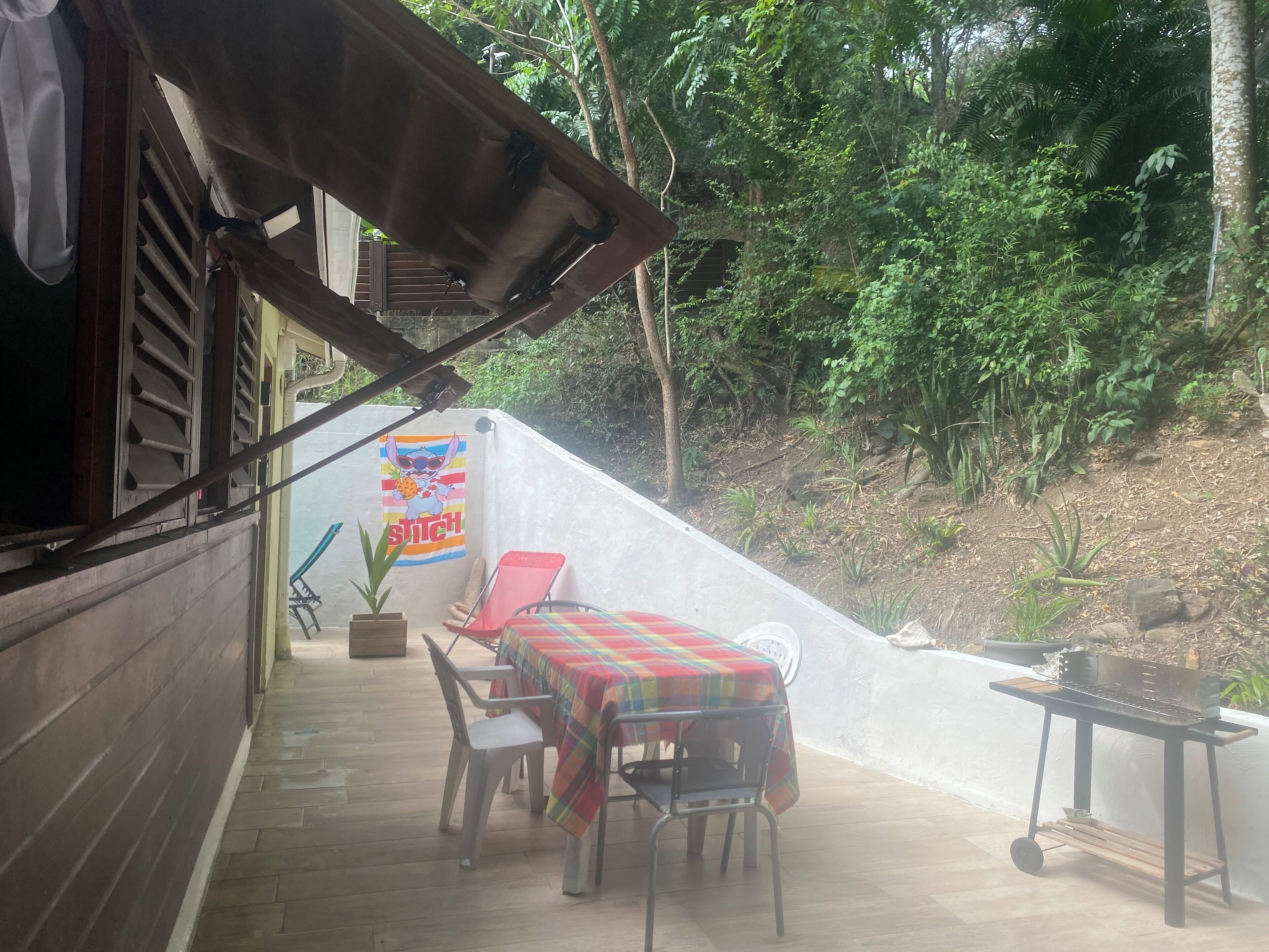 Une terrasse extérieure avec une table et des chaises, un barbecue et une affiche accrochée au mur.