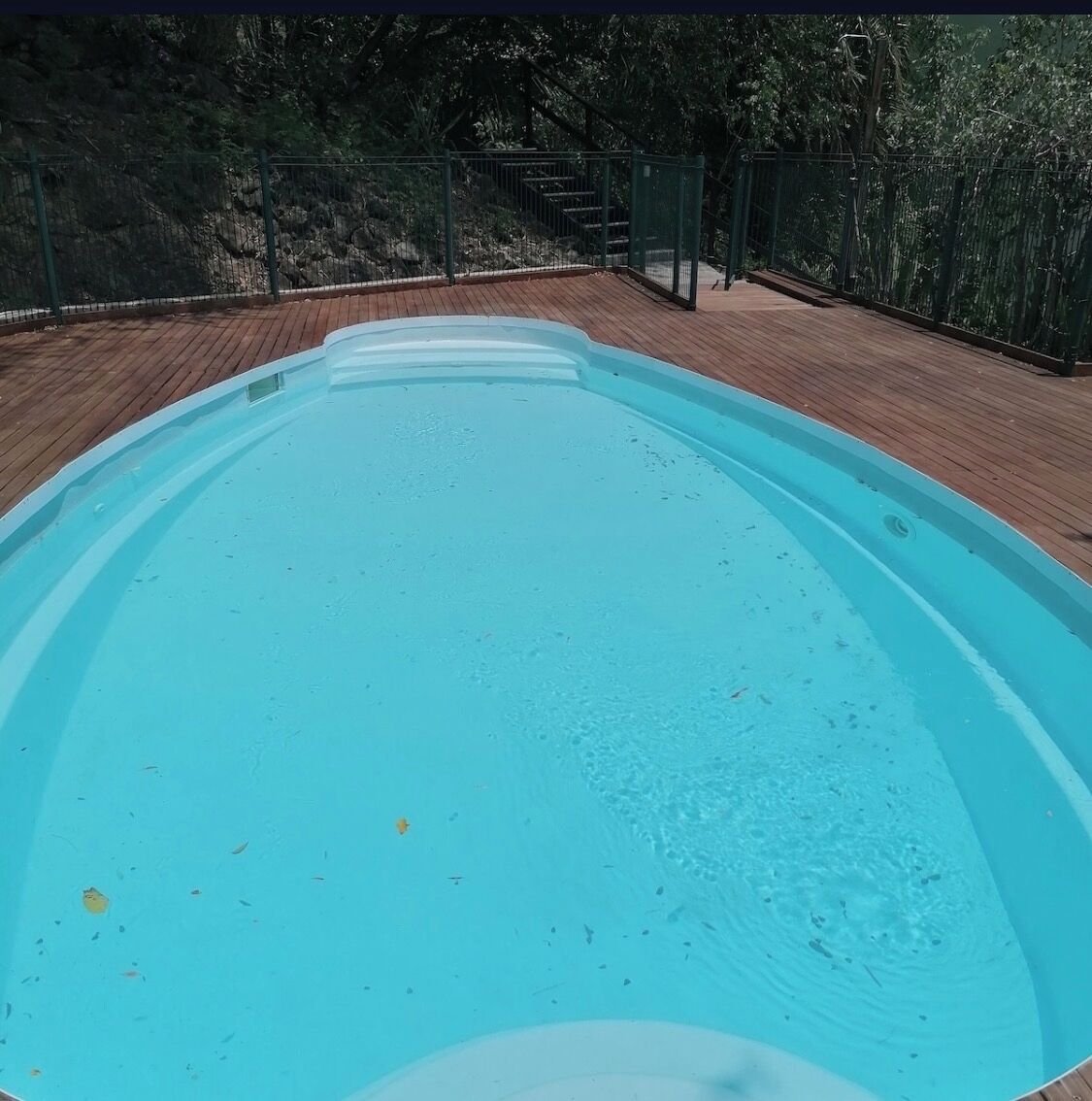 Una piscina vacía con un muelle de madera y una valla metálica.