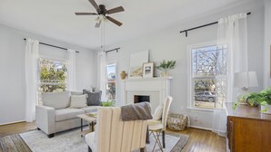 A living room with a sofa, armchair, fireplace, and large windows. - Quaint and Cozy Historic Home in Downtown Weatherford (Weatherford)