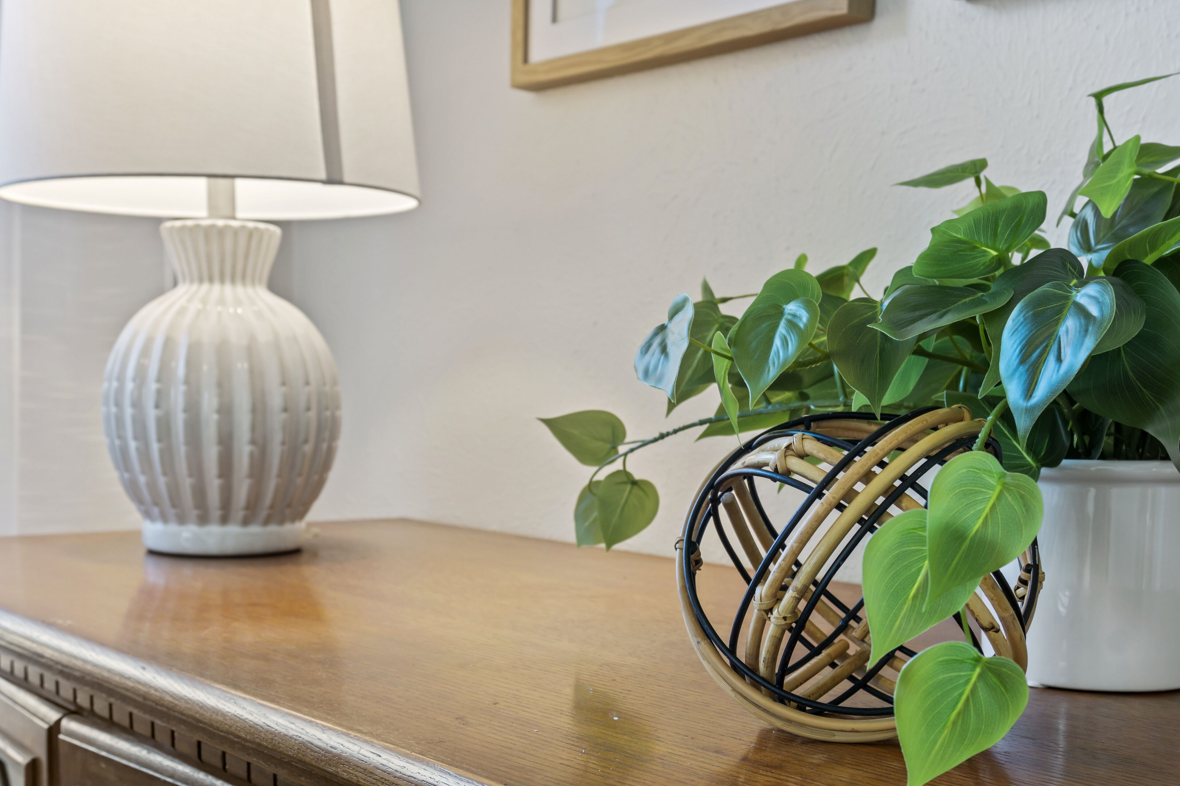 A wooden table with a white vase and a wicker basket containing green plants.
