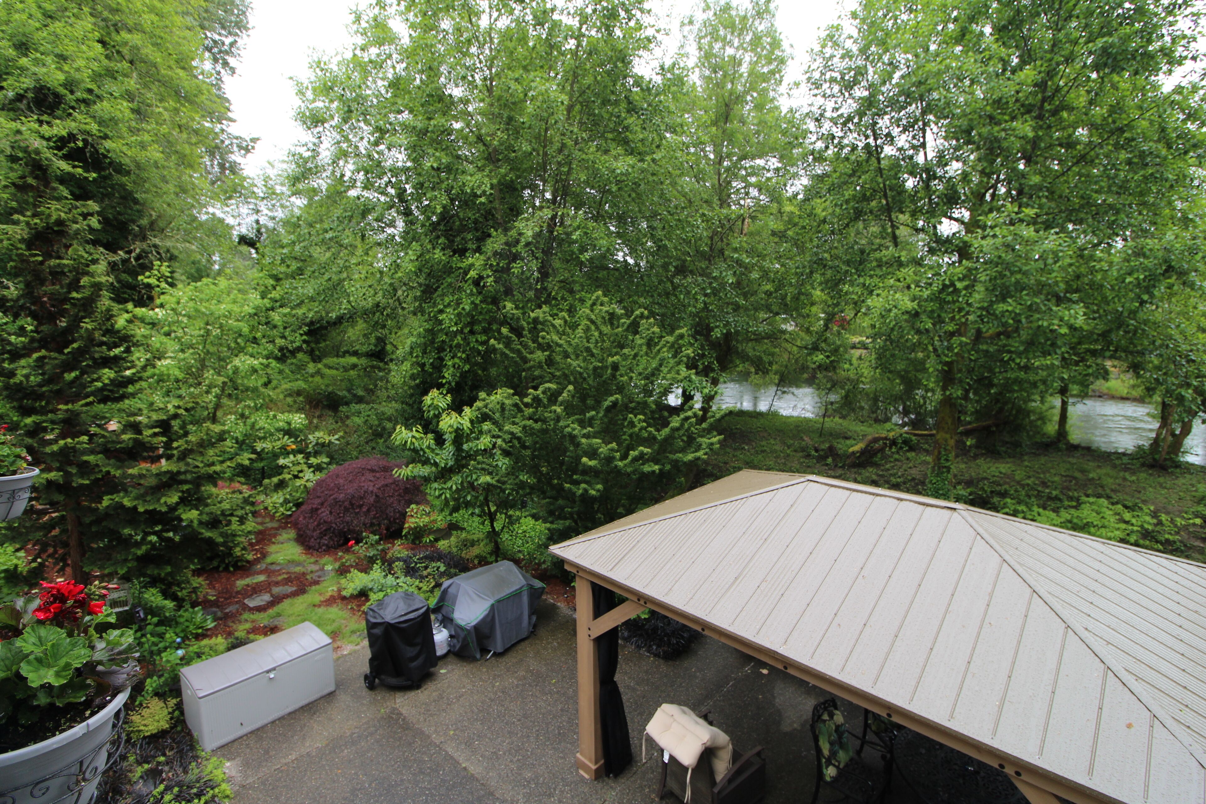 A covered patio area with a view of a wooded area and a body of water.