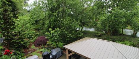 A covered patio area with a view of a wooded area and a body of water.