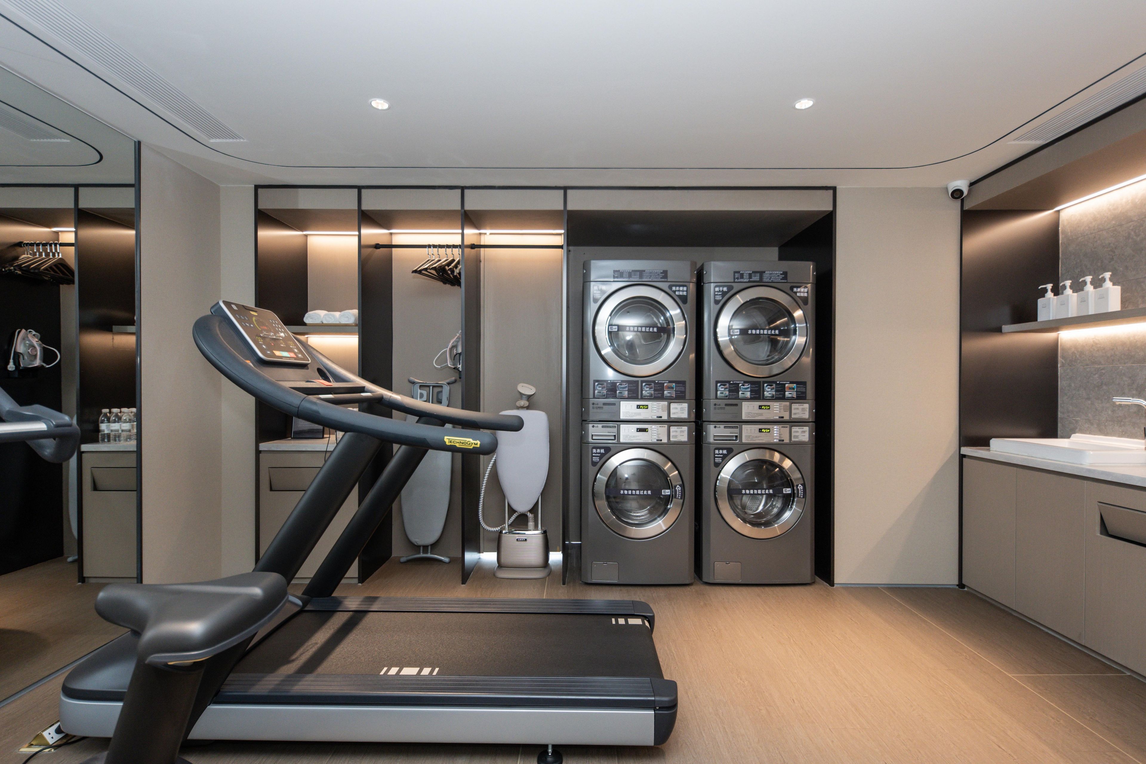 A modern hotel room with a treadmill, a washing machine, and a neatly organized bathroom.