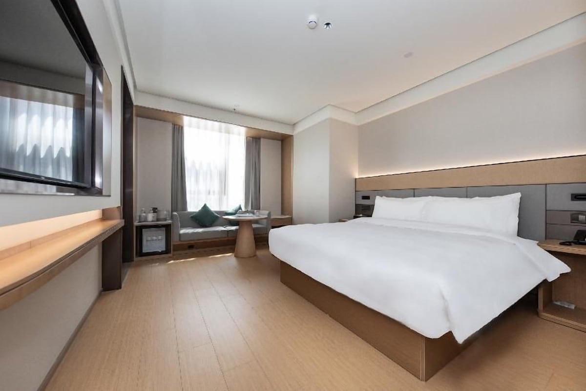 Een moderne hotelkamer met een groot bed, nachtkastjes, een bureau en een zithoek met een bank en een kleintje tafel.