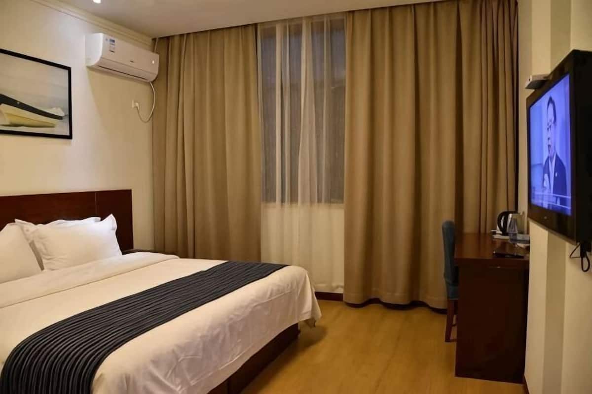 Una habitación de hotel con cama, escritorio, televisor y ventana con cortinas.