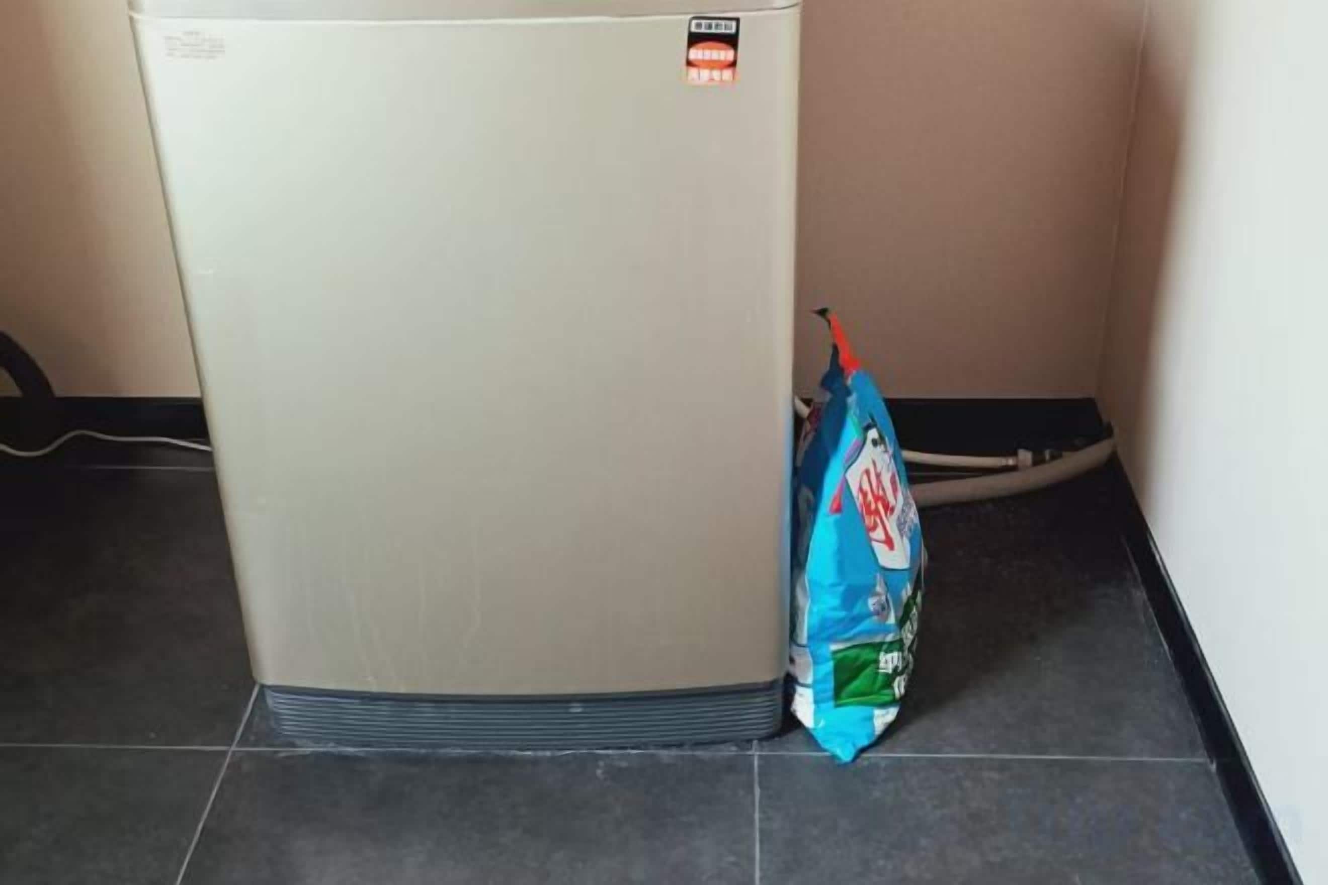 A corner of a room with a white appliance, possibly a refrigerator, and a blue bag on the floor.