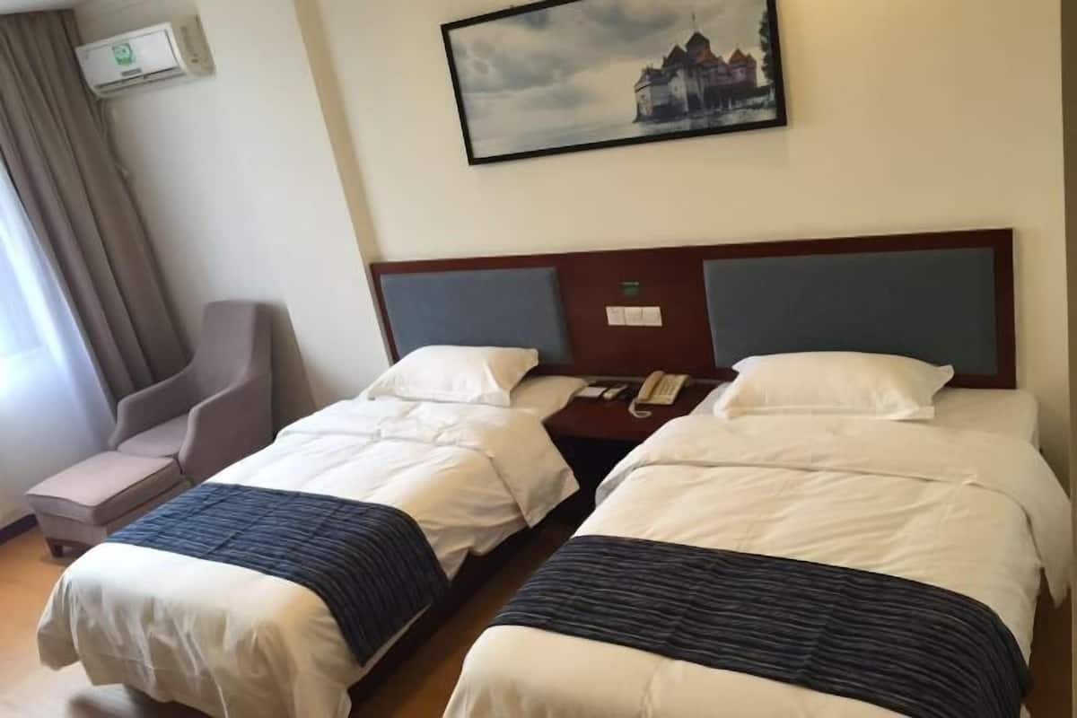 Una habitación de hotel con dos camas, una silla, una mesita de noche con teléfono y un cuadro en la pared.