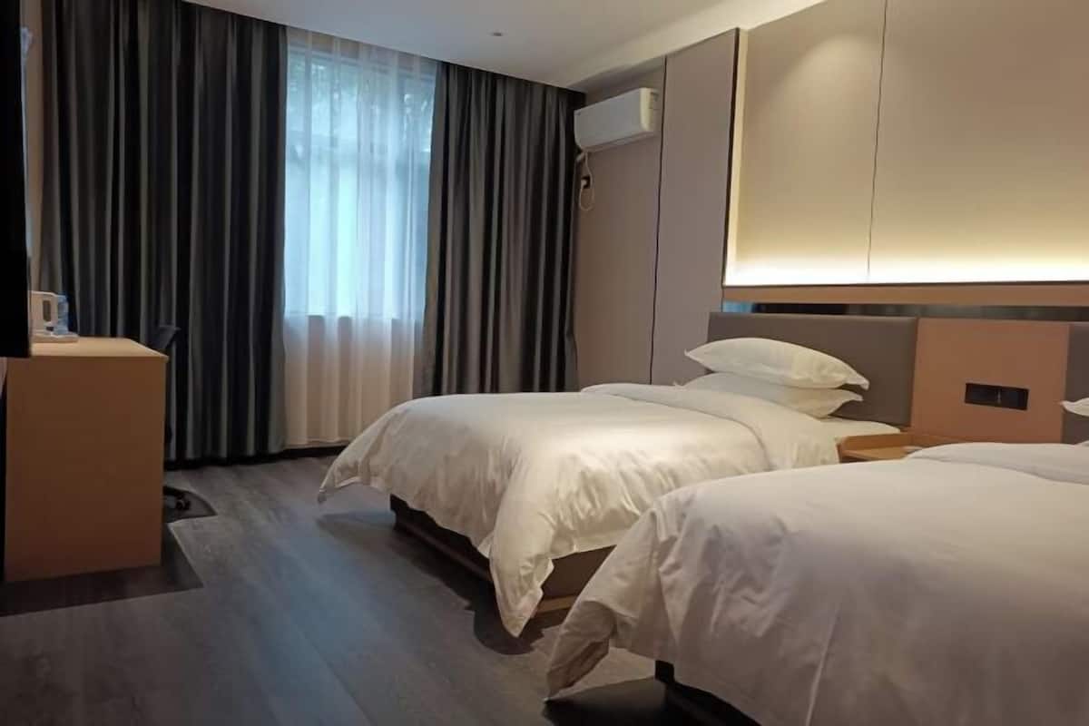Habitación de hotel con dos camas, un escritorio y una ventana con cortinas.