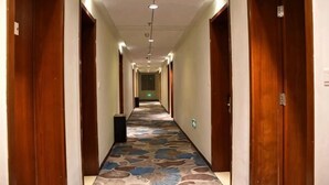 Un pasillo de hotel con puertas de madera, alfombra estampada e iluminación empotrada.