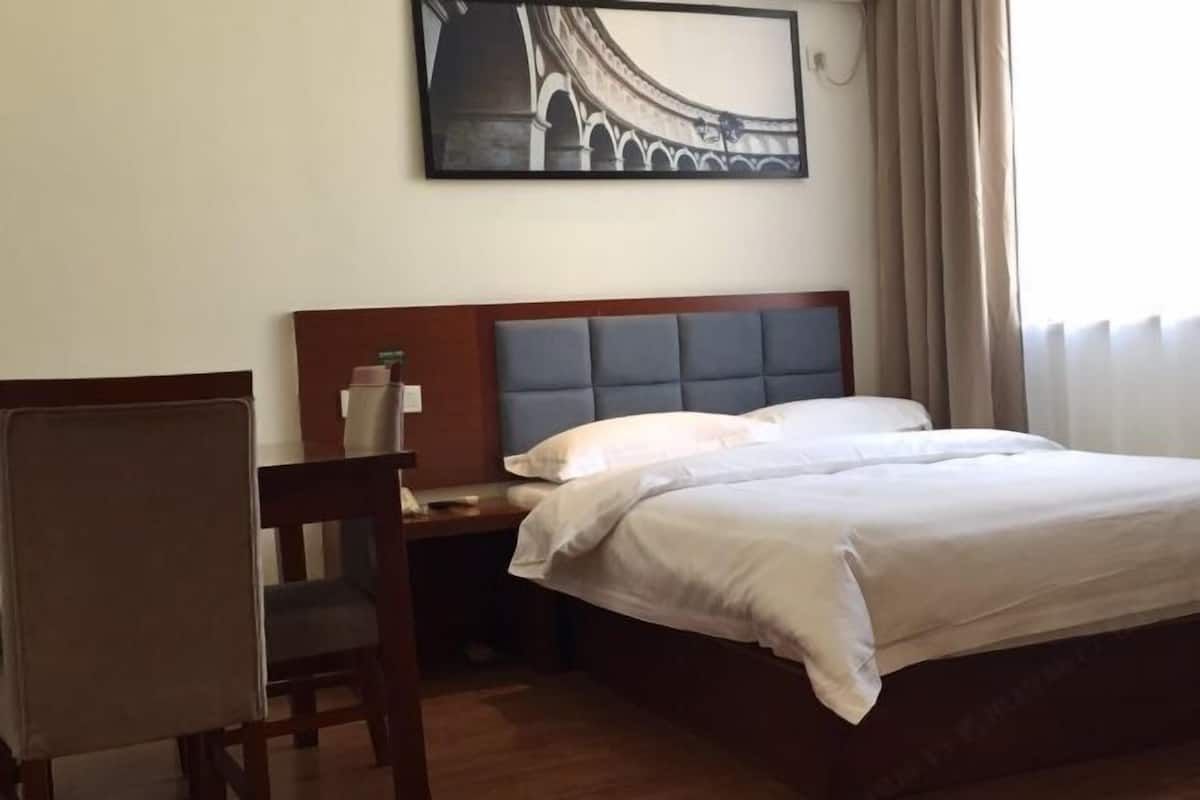 Una habitación de hotel con cama, escritorio, silla y un cuadro en la pared.