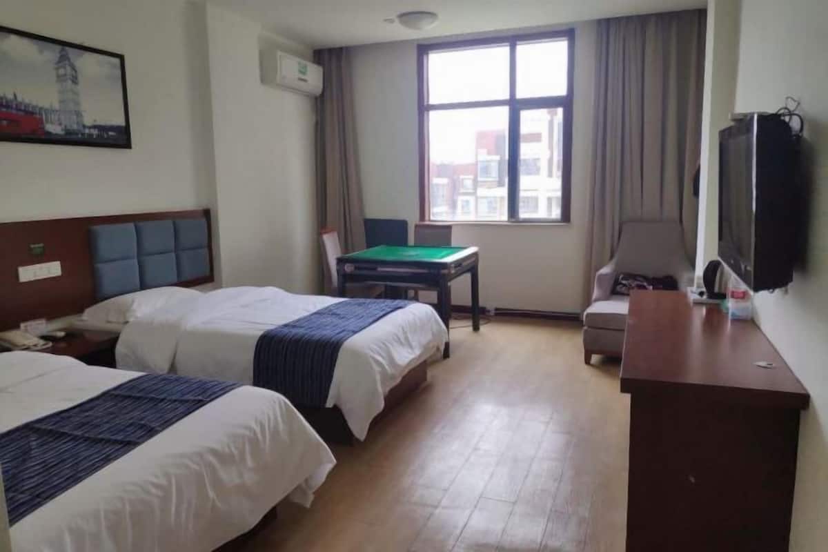 Habitación de hotel con dos camas, un escritorio, una silla, un televisor y un ventanal con cortinas.