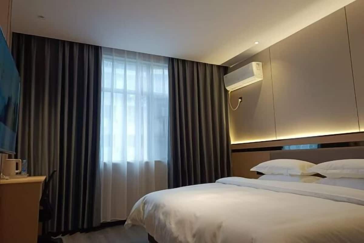 Habitación de hotel con una cama grande, un escritorio con una silla y una ventana con cortinas.