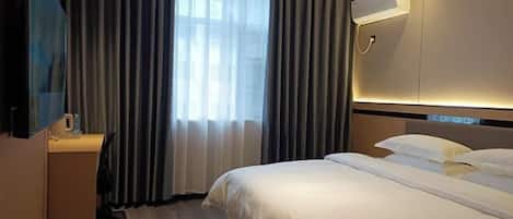 A hotel room with a bed, a desk, a television, and a window with curtains.