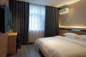 A hotel room with a bed, a desk, a television, and a window with curtains.
