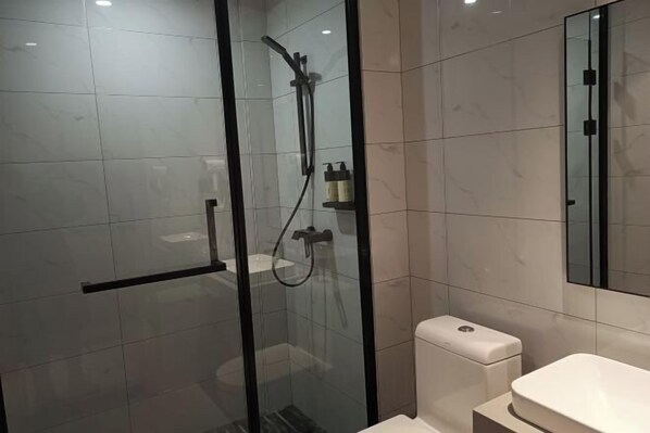 A modern bathroom with a glass-enclosed shower, a toilet, and a sink.