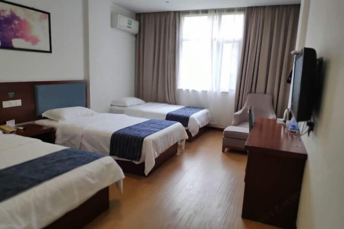 Habitación de hotel con tres camas, un escritorio, una silla, un televisor y una ventana con cortinas.