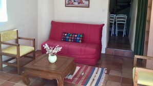 A living room with a red sofa, a wooden coffee table with a vase, and a colorful cushion. A painting hangs on the wall, and a staircase is visible in the background. - 2* gîte on the ground floor of an old pottery in the center of Dieulefit (Dieulefit)