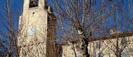 Ein historisches Gebäude mit einem Glockenturm, umgeben von kahl stehenden Bäumen.