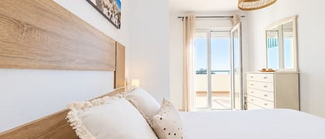 A bedroom with a large bed, a wooden headboard, a hanging rattan light fixture, and a view of the outdoors through a sliding door.