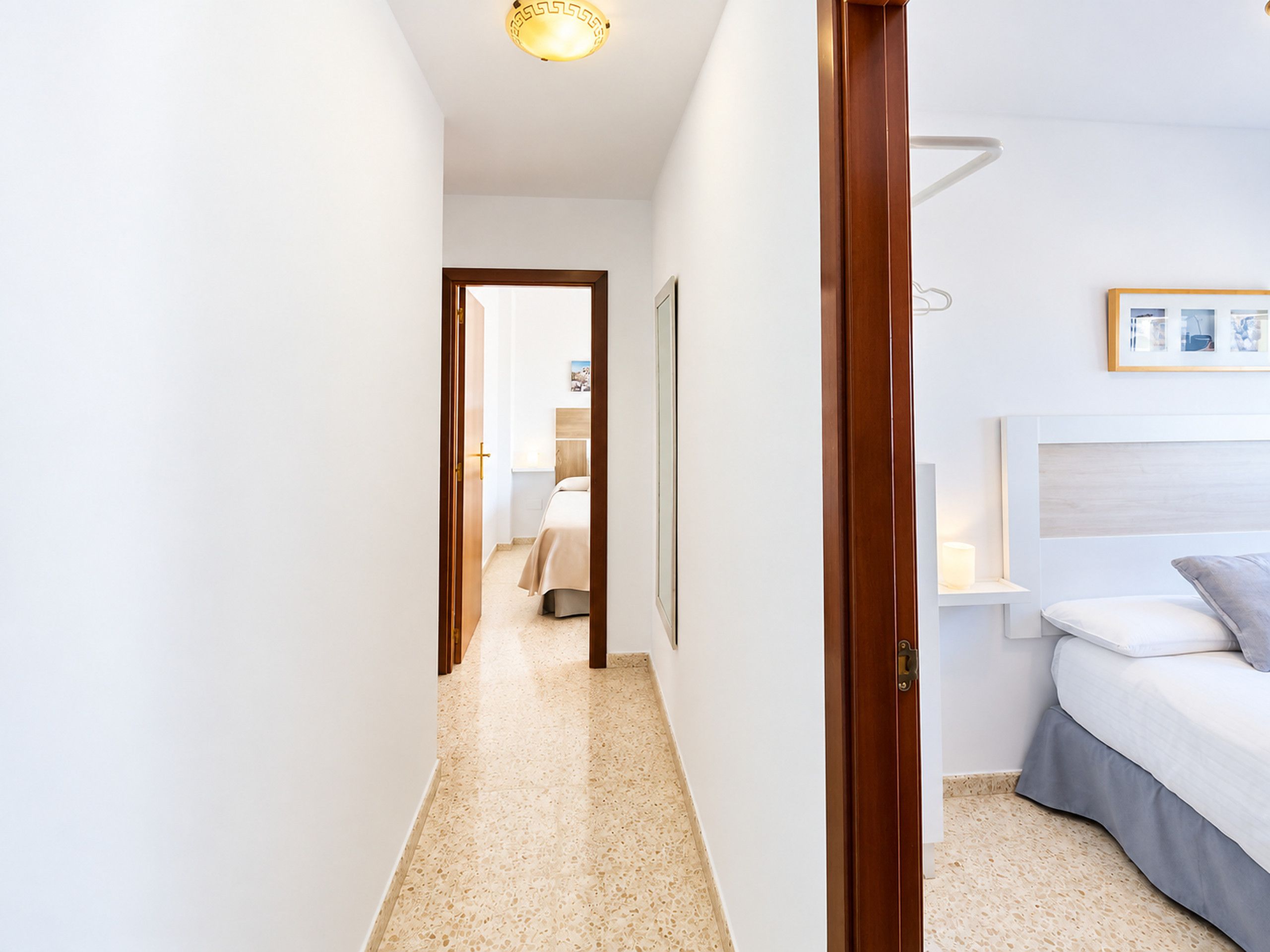 A hotel room with a bed, a bedside table, a nightstand, and a wall-mounted light fixture.