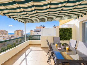 A balcony with a glass table, chairs, and a striped awning.