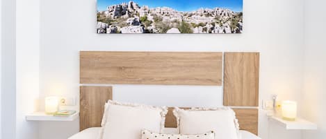 A bedroom with a bed, pillows, a wooden headboard, bedside tables, and a wall-mounted picture.