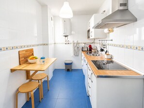 A compact kitchen with a wooden table, two stools, a sink, and a stove.