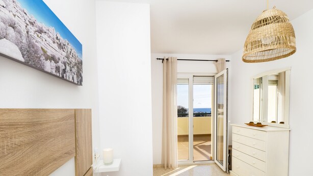 A bedroom with a wooden headboard, a bedside table with a candle, a large window, a balcony with a view, and a hanging wicker light fixture. - Cubo’s La Terraza del Mar / free wifi / sea views (Algarrobo)