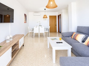 Ein modernes Wohnzimmer mit einem grauen Sofa, einem weißen Couchtisch und einem Essbereich mit Tisch und Stühlen.