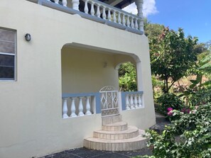Um edifício com fachada branca, uma varanda com grades brancas e um pequeno lance de degraus até a entrada.