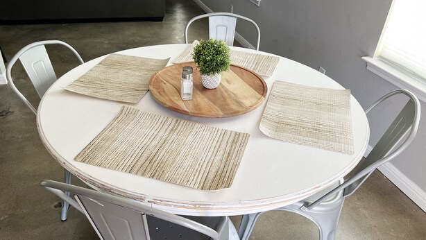 A round dining table with a wooden center, surrounded by four white chairs with gray accents.