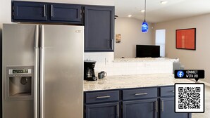 A modern kitchen with dark cabinets, a stainless steel refrigerator, a built-in water dispenser, and a coffee maker.