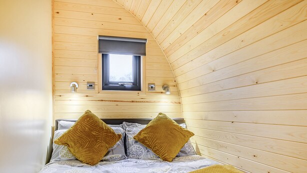A cozy bedroom with wooden walls, a window, and a bed with patterned bedding and two pillows. - Unwind in a relaxing a fun accommodation in a beautiful rural setting. (East Haddon)