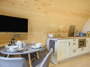 A cozy, compact kitchen with wooden walls, a dining area with a table set for two, and a flat-screen TV mounted on the wall.