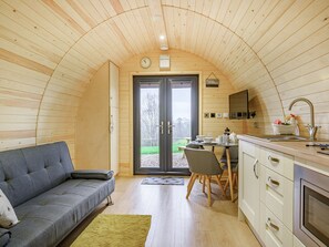 A cozy cabin interior with a wooden ceiling, a sofa, a dining table with chairs, a kitchen area, and a sliding glass door leading to a garden. - Unwind in a relaxing a fun accommodation in a beautiful rural setting. (East Haddon)