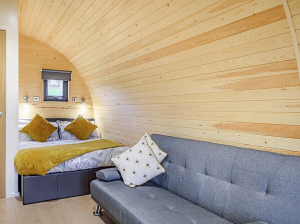 Une chambre confortable avec un lit, un canapé gris, des murs en bois et une fenêtre.