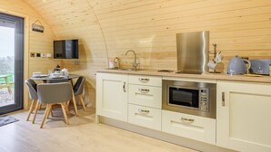 A modern kitchen with wooden paneling, a dining area with a table and chairs, and a view through a large window. - Unwind in a relaxing a fun accommodation in a beautiful rural setting. (East Haddon)