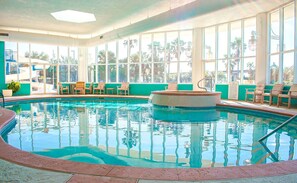 An indoor swimming pool with clear blue water, surrounded by large windows and wooden lounge chairs. - Newly Renovated Condo with Bay Views! Complimentary Boat Slip! (Orange Beach)