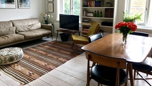 A living room with a sofa, a TV, a bookshelf, and a dining table with chairs. - Stylish Notting Hill flat near Portobello Road (London)