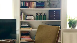 A living room with a brown armchair, a TV on a stand, and a bookshelf filled with books and decorative items. - Stylish Notting Hill flat near Portobello Road (London)