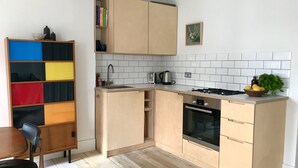 A compact kitchen with wooden cabinets, a Bosch oven, a sink, and a small dining area with a chair. - Stylish Notting Hill flat near Portobello Road (London)