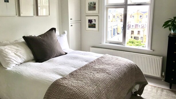 A neatly made bed with a patterned blanket, a window with a view of buildings, and a radiator. - Stylish Notting Hill flat near Portobello Road (London)